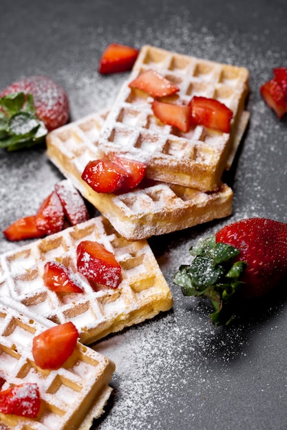 Waffers del Belgio con le fragole e lo zucchero in polvere sul bordo nero.