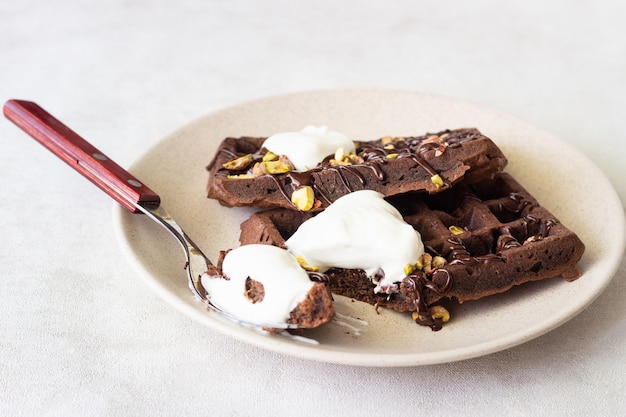 Waffle al cioccolato con cioccolato fuso, pistacchi e panna montata.