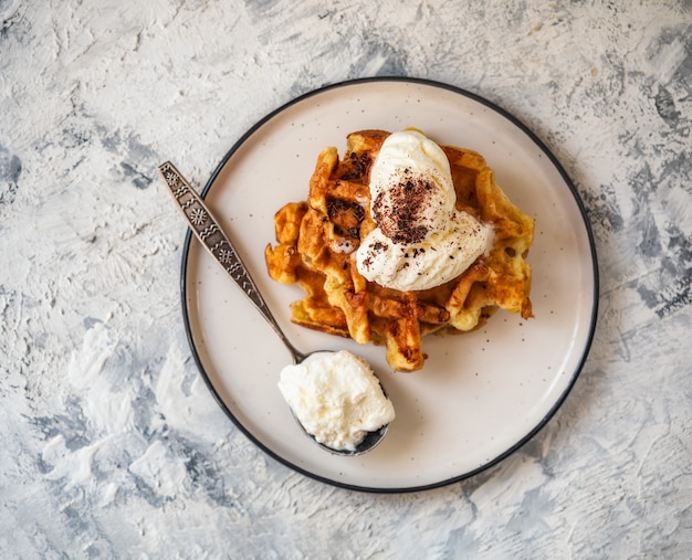 Waffle alla ricotta con gelato e cioccolato grattugiato su un piatto leggero con un cucchiaio