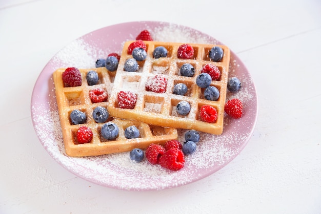 Waffle belgi con mirtilli, lamponi e zucchero in polvere. Concetto di cibo gustoso e sano.