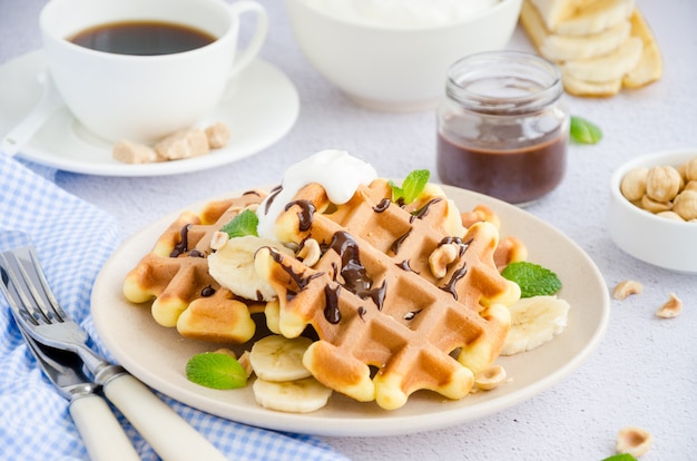 waffle con banana fresca, nocciole, salsa al cioccolato e panna montata su un piatto