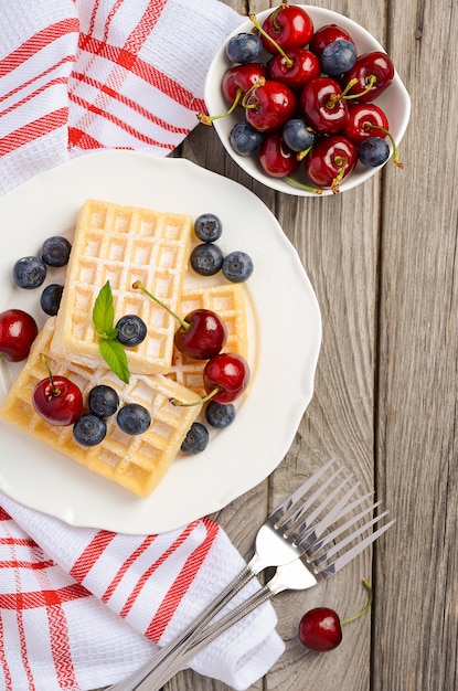 Waffle con ciliegie fresche e mirtilli su un tavolo di legno rustico