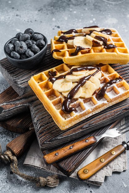 Waffle tradizionali belgi con banana fresca e salsa al cioccolato. Sfondo grigio. Vista dall'alto.