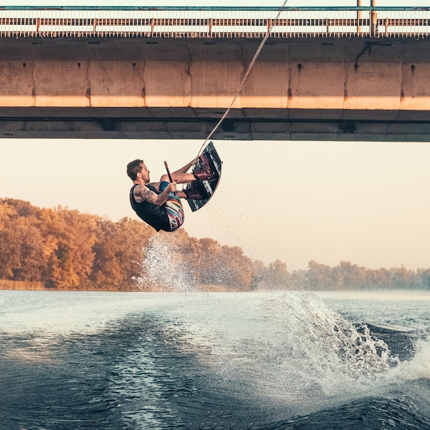 Wakeboarding, l'uomo wakeboarder fa il backflip trick sul fiume sotto il ponte. mattina