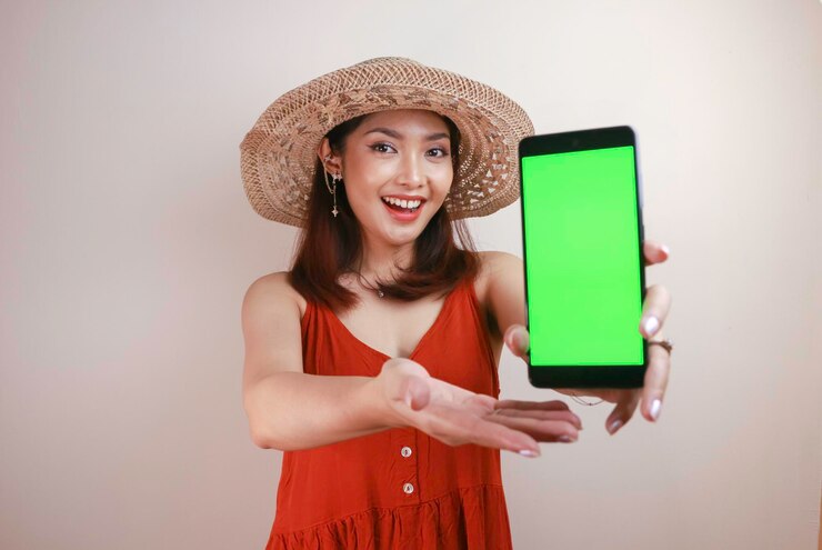 Wanita Asia muda yang bersemangat dan tersenyum menunjukkan layar hijau di ponsel cerdas di tangannya