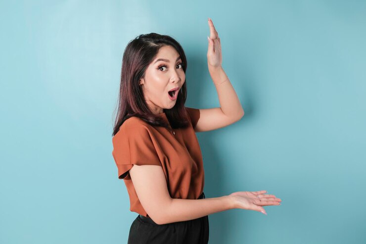 Wanita Asia terkejut menunjuk ruang kosong di sampingnya dan tersenyum diisolasi dengan latar belakang biru