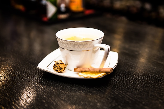 Warming cocktail alcolico in una tazza bianca, la barra con un bastoncino di cannella e un'arancia arancione