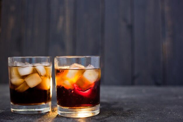 Whisky o rum con cola e ghiaccio in bicchieri su uno sfondo scuro