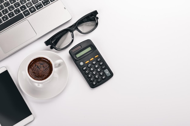 White Office Desk Laptop telefono tazza di caffè occhiali penna matita su sfondo bianco Vista dall'alto Spazio libero per il testo