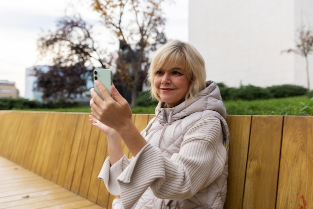 Wi-Fi gratuito nel parco cittadino ritratto di una donna caucasica sorridente adulta seduta su panchina e videochiamate