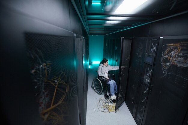wide angle portrait of disabled woman in wheelchair working with supercomputer network in server room, accessible job concept, copy space