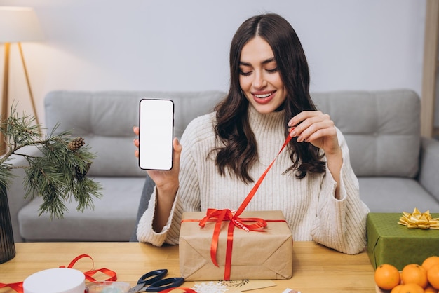 Woman doing New Year or Christmas gift wrapping while holding smart phone
