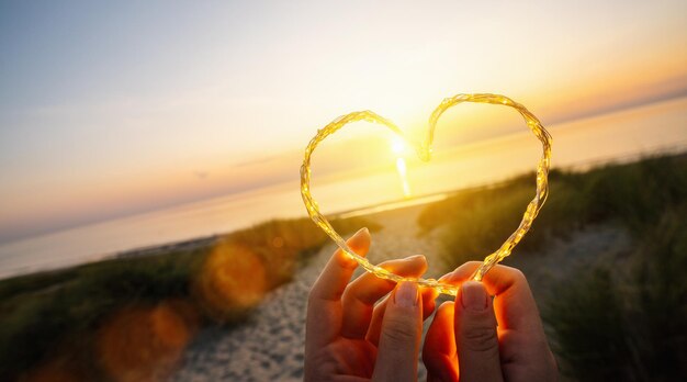Womand holding Forma del cuore fatta di luci a led sulla spiaggia vicino al mare copyspace per il tuo testo individuale