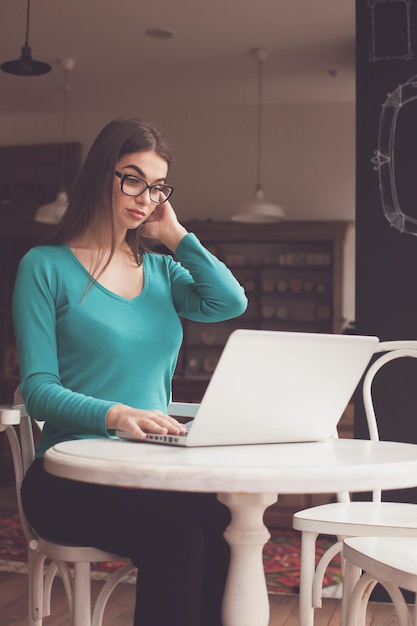 Womanfreelancer con occhiali neri sta lavorando con il suo laptop grigio al tavolo di legno