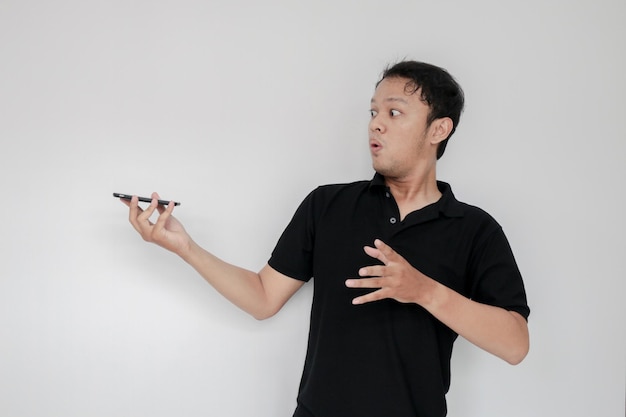 Wow, il volto del giovane asiatico ha scioccato ciò che vede nello smartphone su uno sfondo grigio isolato