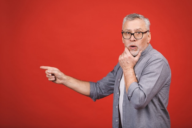 Wow! Incredibile! Uomo senior colpito invecchiato che indossa i vetri, presentando con la mano e indicando con il dito.