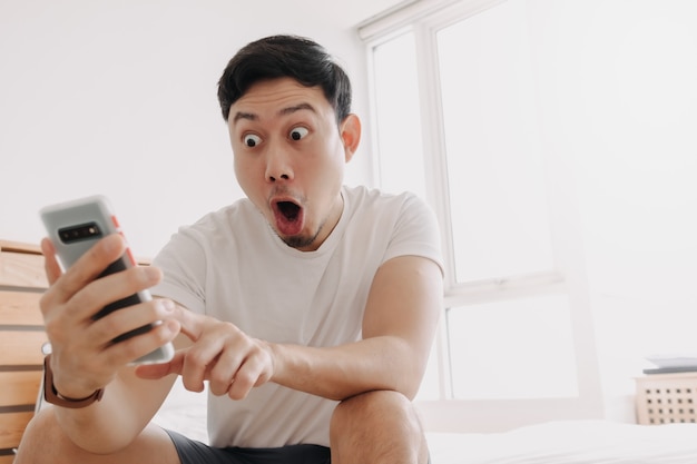 Wow, la faccia di un uomo sorpreso mentre guarda lo smartphone nel suo appartamento