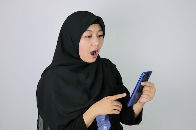 Wow La giovane donna asiatica dell'Islam che indossa il velo è scioccante ciò che vede sullo smartphone Donna indonesiana su sfondo grigio