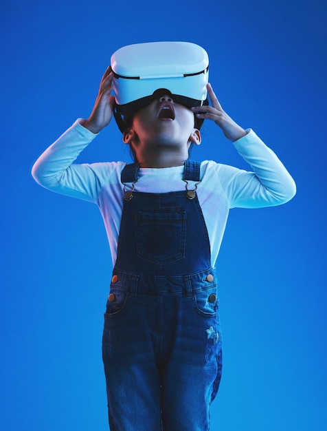 Wow ragazza e bambino con occhiali per realtà virtuale futuristici e metaverso su uno sfondo blu studio Bambino e modello con visore vr futuro e giochi online con espressione e tecnologia