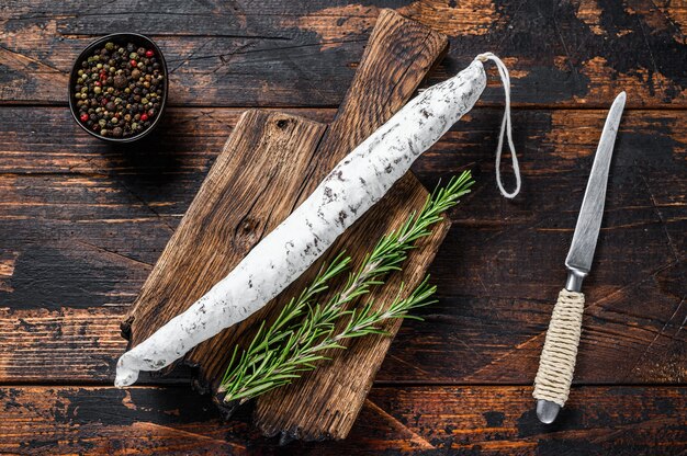 Wurst di salame spagnolo Fuet su un tagliere di legno. Fondo in legno scuro. Vista dall'alto.