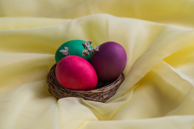 XAa nido marrone con uova dipinte multicolori si erge su uno sfondo di tessuto giallo Decorazione pasquale Decorazioni pasquali primaverili