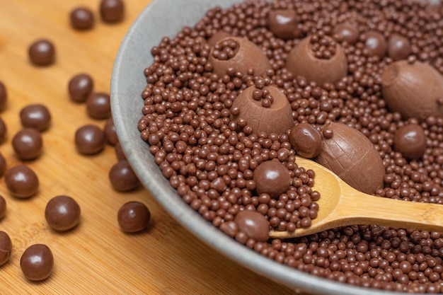 XAdiversi tipi di palline di cioccolato in una ciotola grigia con un cucchiaio pieno di cioccolato