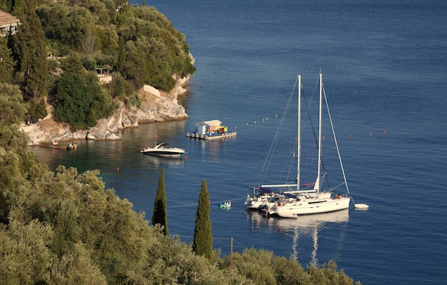 Yacht bianco ormeggiato in mare vicino alla costa rocciosa isola di Corfù Grecia vacanze estive vacanze