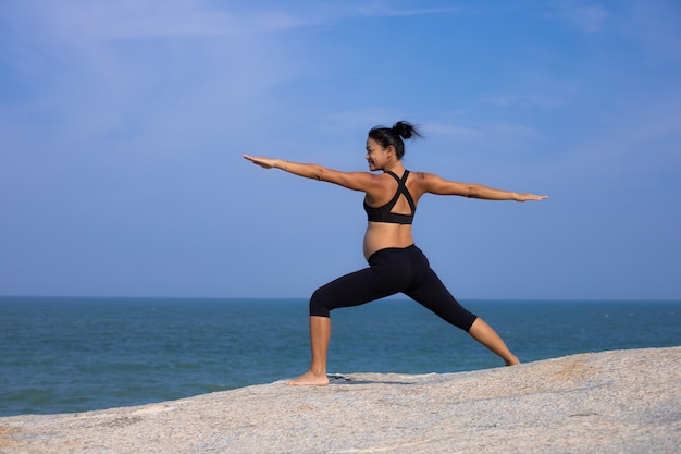 Yoga asiatica della donna incinta sull'ora legale di tramonto della spiaggia