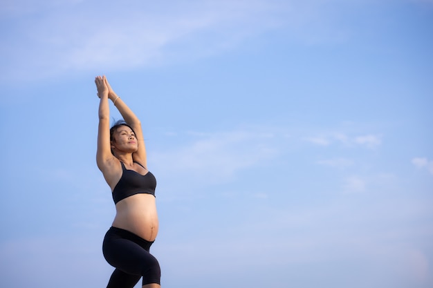 Yoga asiatica della donna incinta sull'ora legale di tramonto della spiaggia