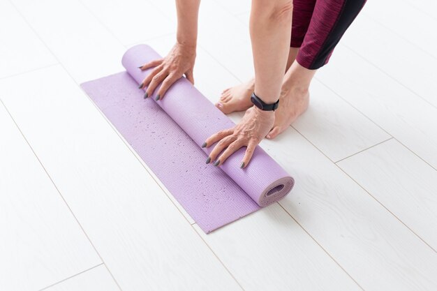 Yoga, concetto di persone - Close up della donna che rotola la sua stuoia dopo una lezione di yoga