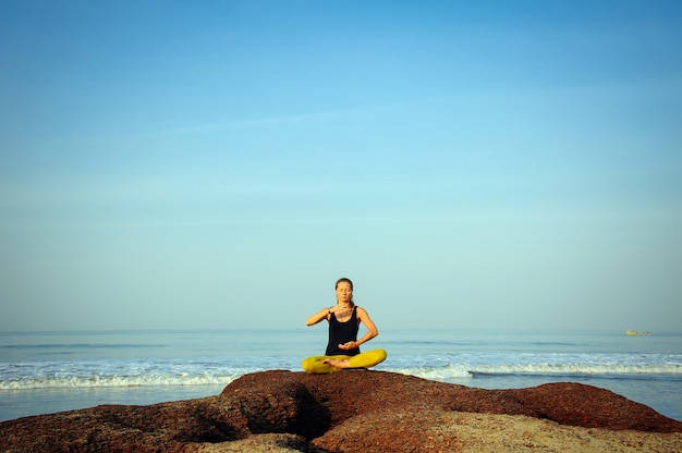 Yoga di pratica della bella giovane donna ed esercizi di allungamento alla spiaggia dell'oceano di estate.