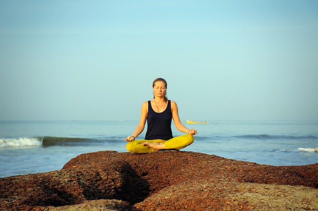 Yoga di pratica della bella giovane donna ed esercizi di allungamento alla spiaggia dell'oceano di estate.
