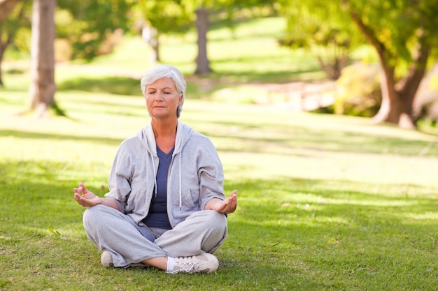 Yoga di pratica della donna senior nel parco