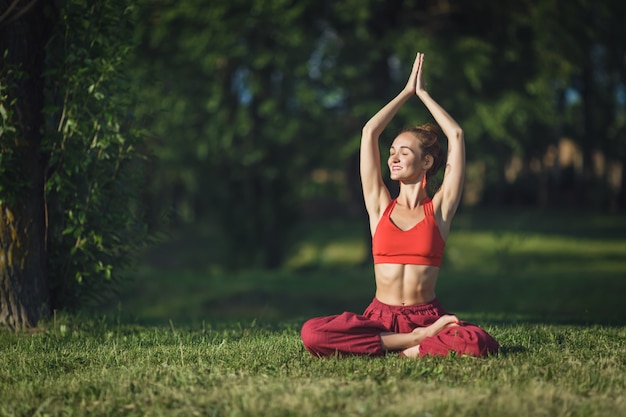 Yoga di pratica della giovane donna all'aperto. La femmina medita all'aperto nel parco della città dell'estate.