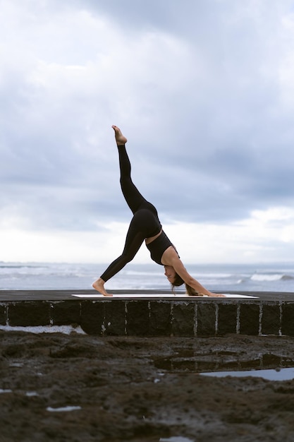 Yoga di pratica della giovane donna su una bella spiaggia all'alba. Cielo blu, oceano, onde, vicinanza alla natura, unità con la natura.