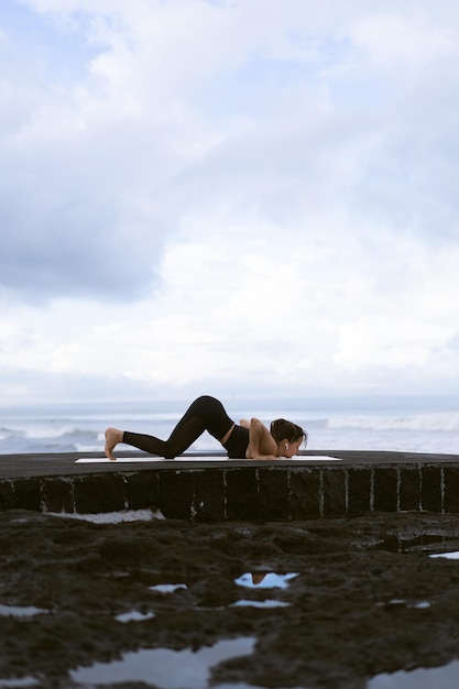 Yoga di pratica della giovane donna su una bella spiaggia all'alba. Cielo blu, oceano, onde, vicinanza alla natura, unità con la natura.