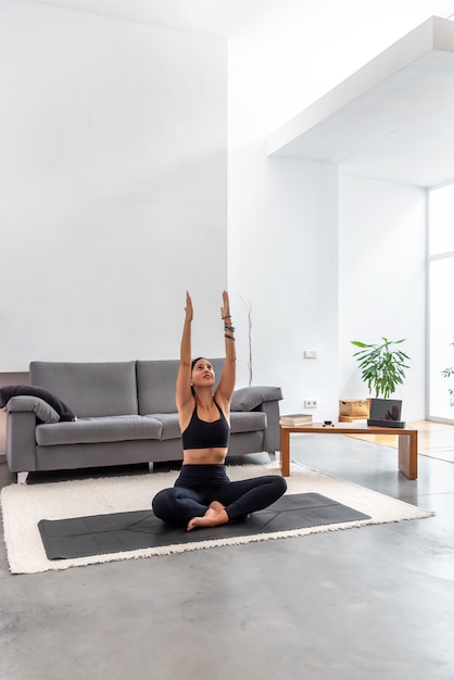 Yoga di pratica della giovane donna sul suo salone luminoso a casa