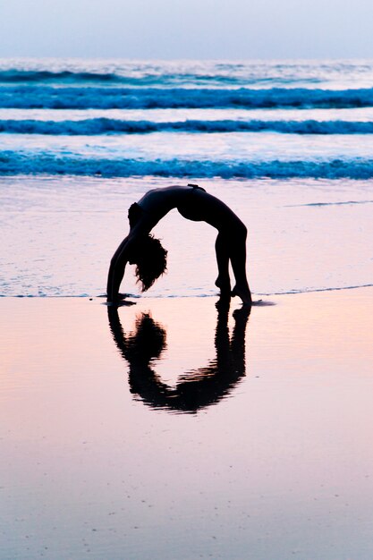 Yoga di pratica della giovane donna sulla spiaggia a Agonda, Goa, India