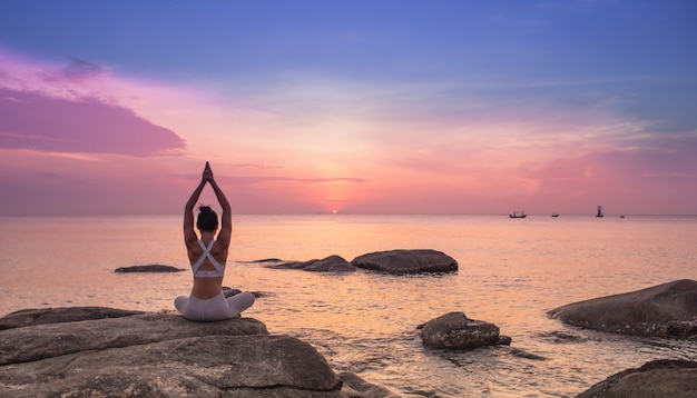 Yoga di pratica della ragazza su una roccia