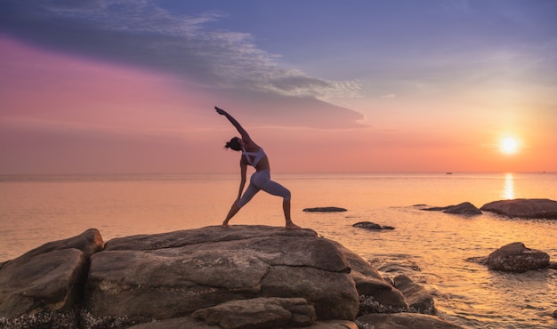 Yoga di pratica della ragazza su una roccia