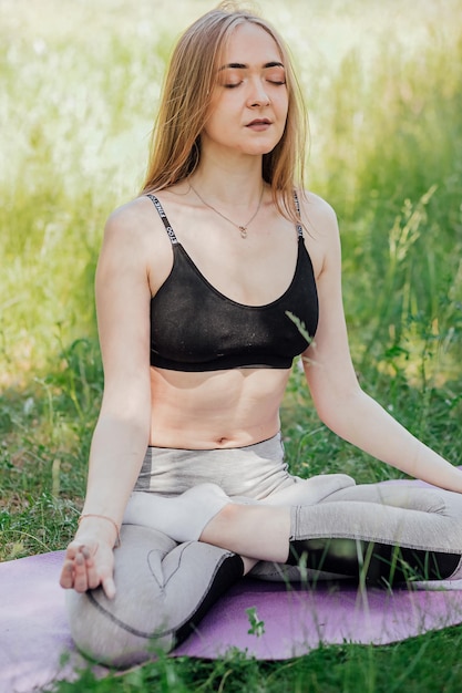 Yoga donna su erba verde ragazza si rilassa nel campo Yoga donna nel parco verde ragazza che fa ginnastica all'aperto Meditando donna in meditazione in posa yoga pratiche all'aperto