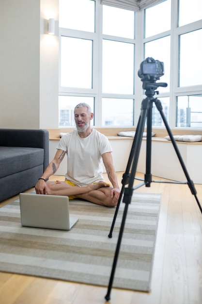 Yoga in linea. Un uomo maturo in maglietta bianca che fa tutorial di yoga online