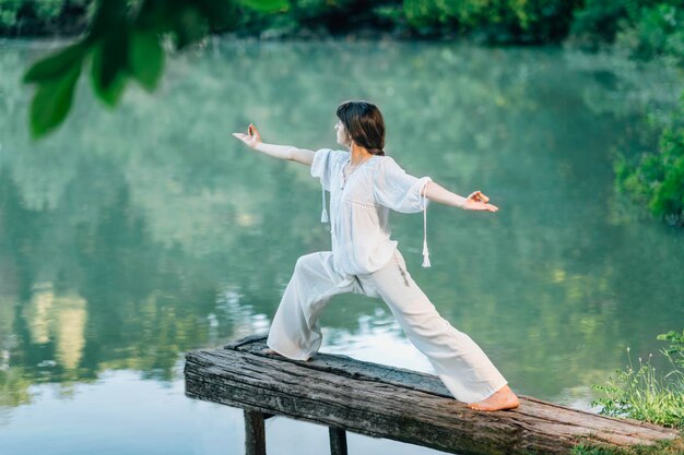 Yoga in riva al lago Giovane donna che pratica la posa del guerriero 2