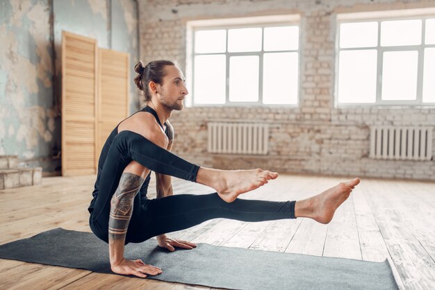 Yoga maschile in palestra, esercizio di equilibrio sulla stuoia