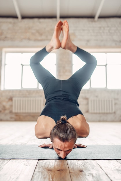 Yoga maschio in piedi sulle mani a testa in giù. Esercizio sulla stuoia in palestra con interni grunge. Allenamento in forma al chiuso