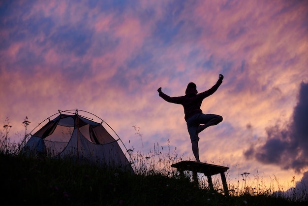 Yoga Mounatain. Siluetta della femmina che medita su banco vicino alla tenda sul pendio di montagna