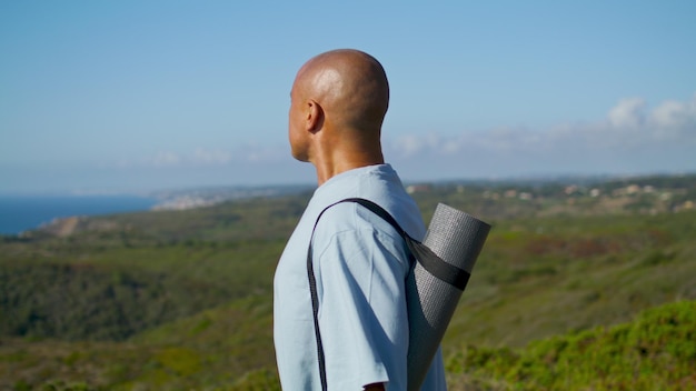 Yoga uomo alla ricerca di mare alla luce del sole Atletico ragazzo tenendo stuoia contemplando la costa