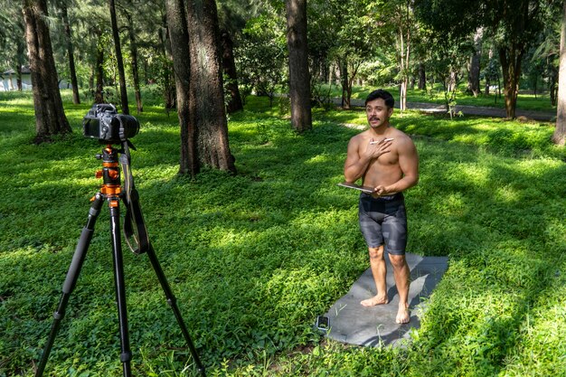 Yogi maschio bello attivo cammina in un parco passeggiando nella foresta prima o dopo un allenamento Giovane uomo atletico ispanico lezione di yoga con un tappetino fitness