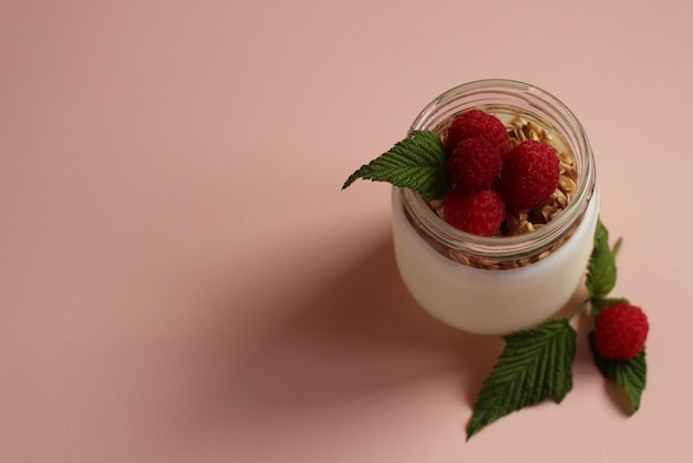 Yogurt bianco naturale in vasetto di vetro con muesli di lamponi su fondo rosa