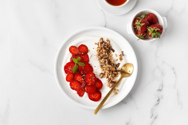 Yogurt con fragole e muesli in piatto bianco Prodotto lattiero-caseario cremoso Vista dall'alto sullo sfondo di marmo